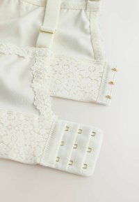 Bandă pentru sutien din dantelă albă cu cârlige aurii și bretele reglabile, care arată modele florale din dantelă și textura țesăturii.