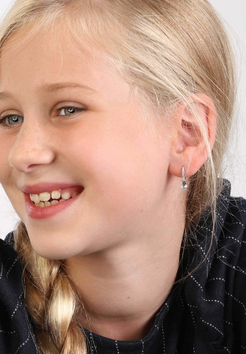 Silberne Creolenohrringe mit klaren Edelsteinakzenten. Das Model hat hellblonde Haare und trägt ein Oberteil mit dunklem Muster.