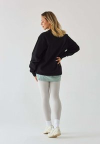 Czarny oversize sweatshirt, miętowa warstwowa koszula, jasnoszare legginsy, białe skarpetki i beżowe sneakersy. Gładkie materiały, swobodny styl.