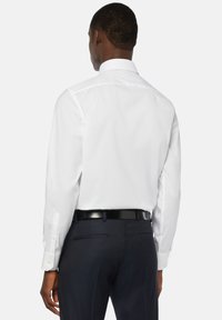 Bela srajca z strukturovnim ovratnikom, dolgimi rokavi in gumbnimi manšeti, v kombinaciji s temno modrimi hlačami in črnim pasom.