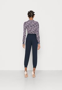 Dopasowane granatowe spodnie z elastycznymi mankietami w połączeniu z kwiecistą bluzką z długim rękawem o wysokim dekolcie i marszczonymi detalami.