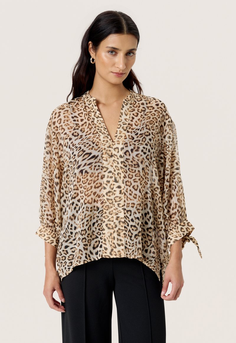 Bluse med leopardprint i gennemsigtigt stof, med V-hals, oprullede ærmer og løs pasform, kombineret med skræddersyede sorte bukser.