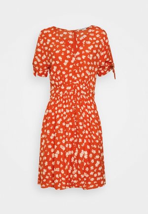 Robe rouge longueur genou avec motif floral blanc, manches courtes avec liens, taille froncée et décolleté goutte d'eau.