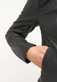 Zwarte leren jas met een aansluitend ontwerp, een gestructureerd oppervlak, een ritssluiting op de zak en licht opgerolde manchetten, die de strakke silhouet benadrukken.