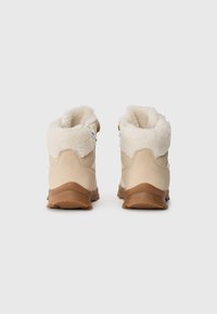 Beige turstøvler med fluffy hvit fôr, rund krage og teksturerte gummisåler. Funksjoner inkluderer en sidelukking og forsterket hæl.