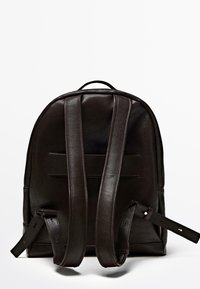 Brown leather backpack with a rounded top, adjustable straps, and a textured finish. Features two vertical seams on the back.