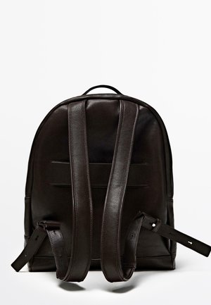 Brown leather backpack with a rounded top, adjustable straps, and a textured finish. Features two vertical seams on the back.