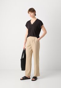 Maglietta nera a V, pantaloni beige con pieghe, sandali neri a incrocio, e una borsa a tracolla nera a coste. Design semplice, texture morbide.