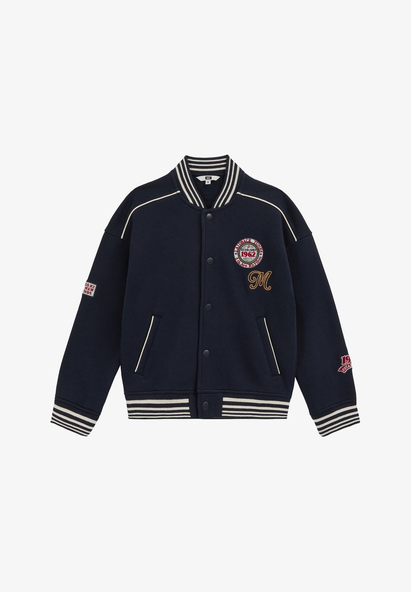 Veste varsity bleu marine avec col, poignets et ourlet rayés blancs, boutons-pression, poches avant et écussons brodés sur la poitrine et les manches.