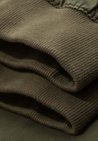 Tela verde oliva plegada con una textura acanalada, que muestra una sensación suave y cálida. El material parece ligeramente difuso y grueso.