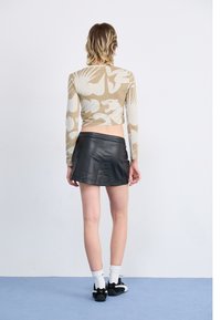 Long-sleeve beige top with white floral and animal patterns, paired with a black faux leather mini skirt. Black sneakers with white accents.