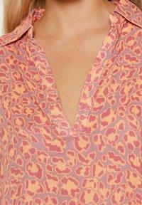 Leopardprint shirt met een diepe V-hals, korte kraag, lichtgewicht stof in pastelroze en paarse tinten, met een zachte textuur.