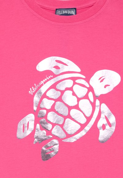 Rózsaszín anyag ezüst fémes tengeri teknős grafikával és a „Vilebrequin” logóval a teknős felett, a gallérnál.