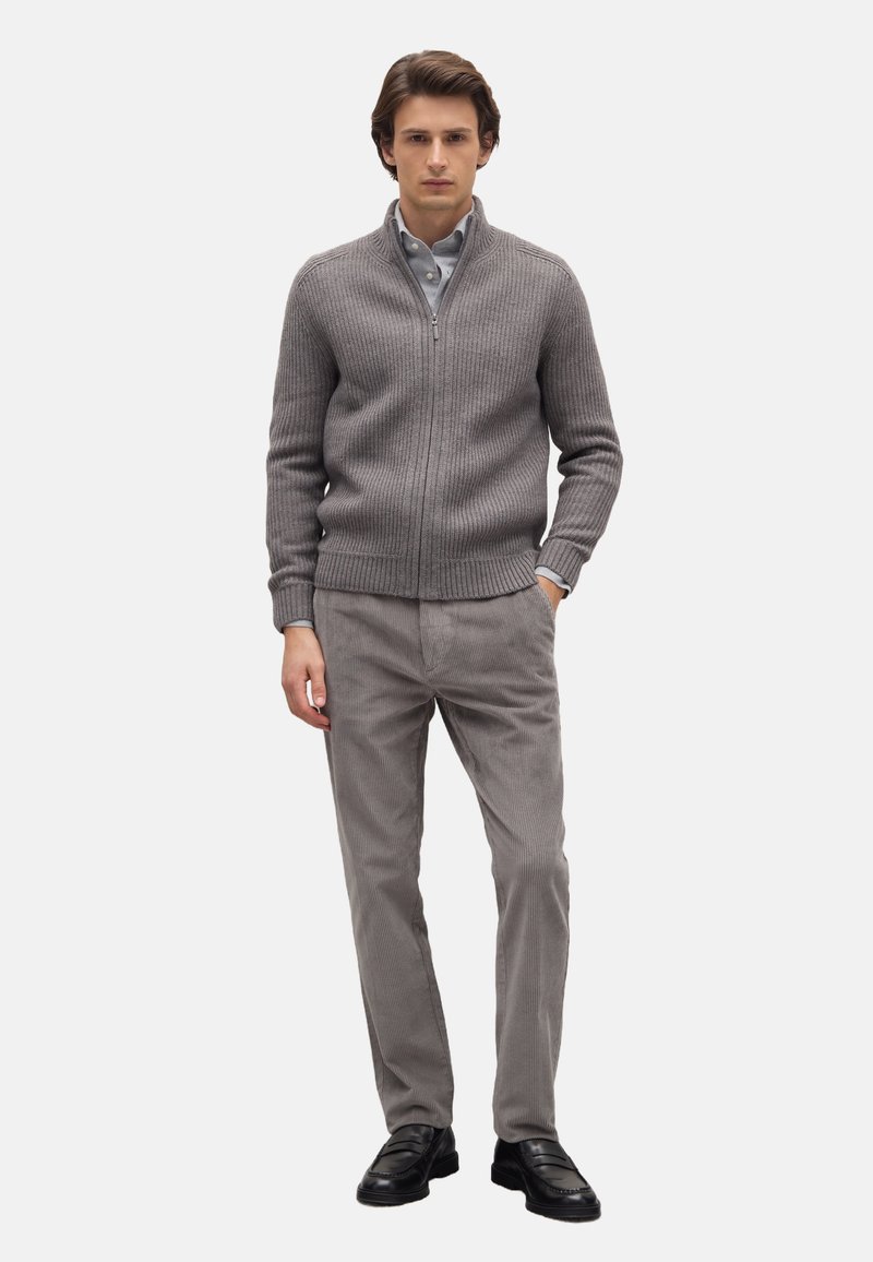 Grijze geribbelde ritstrui over een lichtblauw overhemd, gecombineerd met lichtgrijze ribfluweelbroek en zwarte instapschoenen. Eenvoudige, moderne pasvorm.