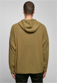 Oliwkowo-zielona dzianinowa bluza z kapturem o prążkowanej strukturze, luźnym kroju i przestronnym kapturze. Posiada długie rękawy i prosty dół.