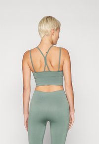 Soutien-gorge de sport vert côtelé avec des fines bretelles et un design croisé dans le dos. Ajusté et raccourci, fabriqué dans un matériau extensible.