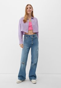 Lichtpaarse cropped button-up shirt over een roze ribbed tanktop, gecombineerd met versleten lichtblauwe wide-leg jeans en witte sneakers.