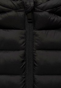 Musta toppatakkimallinen takki, jossa pystysuora vetoketjusuljin, tikattu pinta ja sileä, mattapintainen ulkomateriaali.