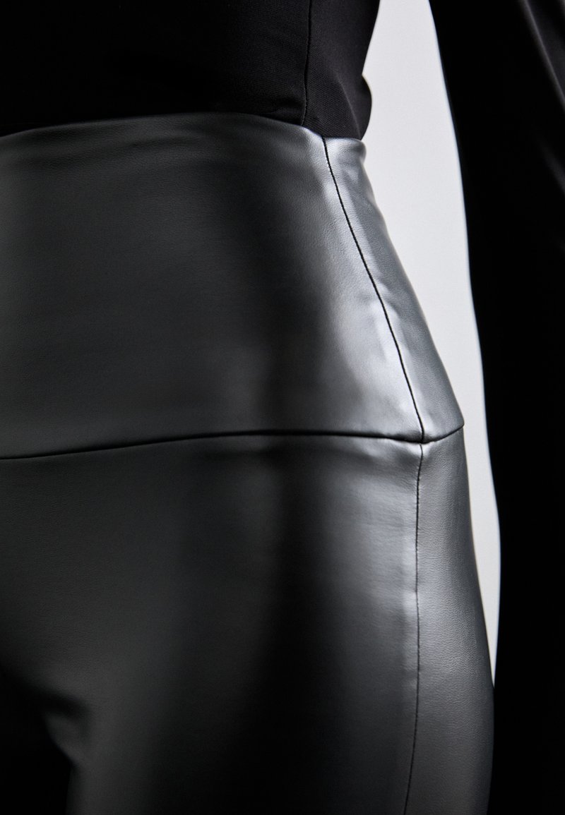 Schwarze Kunstlederhose mit glatter Textur, hohem Bund und klaren Nähdetails. Die schmale Passform betont die Silhouette.