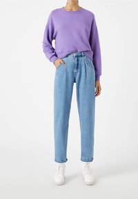 Purpurowy sweatshirt z okrągłym dekoltem i luźnymi rękawami zestawiony z jasnoniebieskimi, wysokim stanem, zwężanymi dżinsami. Białe sznurowane botki dopełniają stylizację.