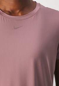 Zbliżenie na osobę w fioletowej koszulce sportowej z małym, pasującym logo Nike poniżej dekoltu.