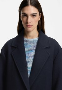 Marinblå ullrock med breda slag, i kombination med en flerfärgad stickad tröja med blå, lila och vita texturer.