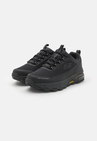 Black waterproof sneakers with a textured mesh upper, padded collar, and thick rubber sole featuring visible cushioning and traction patterns.