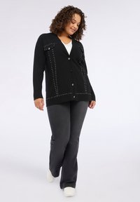 Cardigan negru cu detalii cu bătăi, decolteu in V și închidere cu nasturi. Asortat cu pantaloni gri și adidași albi. Textură netedă.