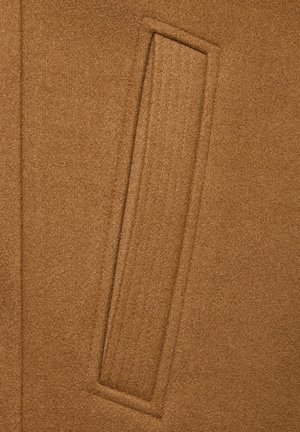 Zbliżenie brązowego wełnianego płaszcza z kieszenią z prostokątnym przeszyciem i otwarciem na krawędzi.