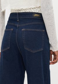 Tmavě modré džíny z denimu se vypasovaným střihem, které mají dvě zadní kapsy a zlatou visačku s logem "ONLY" umístěnou nad pasem.