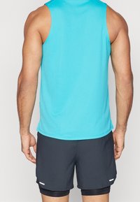 Débardeur turquoise à encolure ronde et coupe sans manches, associé à un short noir avec un détail accent blanc. Texture lisse.