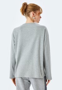 Grauer Langarm-Sweatshirt mit lässigem Schnitt. Weicher, strukturierten Stoff, runder Hals und seitliche Schlitze für mehr Bewegungsfreiheit. Hat ein schlichtes Design.