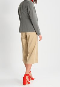 Šedý přiléhavý blazer, béžové široké kalhoty a červené sandály na vysokém podpatku s mašlí. Hladká tkanina, strukturovaný design, neformální styl.