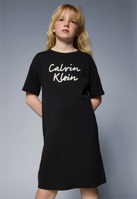 Czarna bawełniana sukienka t-shirt z białym, kursywnym logo "Calvin Klein". Luźny krój, krótkie rękawy i długość do kolan. Gładka faktura.