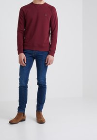 Sudadera burdeos con cuello redondo, puños y dobladillo acanalados; combinada con jeans skinny azules y botas de ante marrón hasta el tobillo.