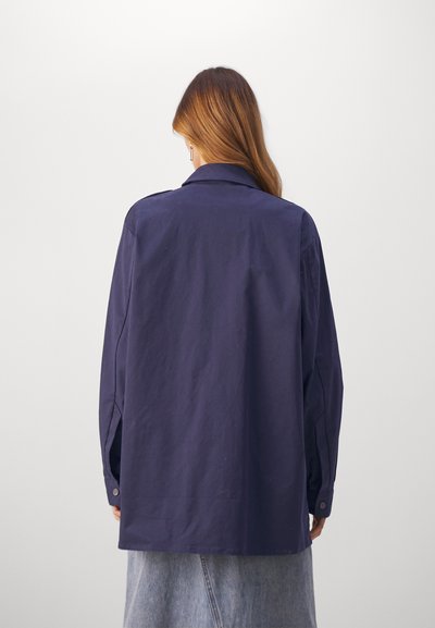 Navyblauw oversized shirt van katoen, voorzien van een knoopsluiting bij de manchetten, puntige kraag en een gladde textuur, gezien van de achterkant.