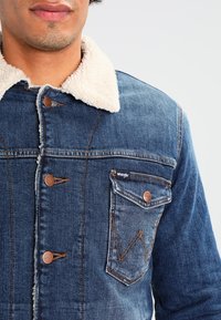 Jeansjacka med sherpa-krage, blå i färgen, med knäppning fram, bröstficka med zigzag-stygn och Wrangler-logotyp.