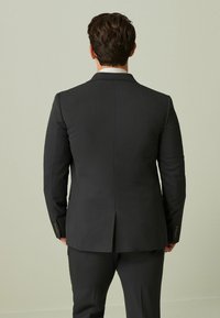 Mørkegrå jakkesæt med slim fit, enkelt ventil bagpå og detaljerede guldbuttons på ærmerne. Glat stofstruktur.