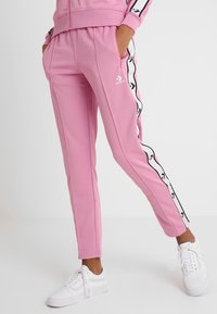 Rosa Sport-Sweathosen mit schmaler Passform, weißen Seitenstreifen mit schwarzen Akzenten und einem elastischen Bund. Weiße Turnschuhe runden das Outfit ab.