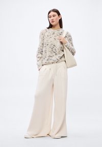 Pulover tricotat crem cu model texturat, asortat cu pantaloni largi bej deschis, finisaj neted și o geantă ușoară.