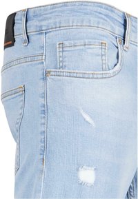 Vaqueros de denim azul claro con un diseño desgastado, bordes deshilachados y detalles en los bolsillos. La tela tiene una textura suave y un acabado casual.