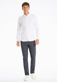 Witte lange mouwen overhemd met knoopjes, donkergrijze chinos en witte sneakers. Eenvoudig ontwerp, gladde stof, op maat gemaakte pasvorm met minimale accenten.