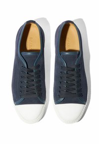 Par obu plavih nubuk tenisica s crnim vezicama i bijelim gumiranim vrhovima, prikazanih odozgo na bijeloj podlozi.