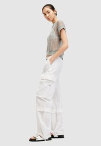 Grijze mesh crop top met korte mouwen, gecombineerd met witte wijde cargo broeken met zakken en koorddetails. Zwarte sandalen met metallic accenten.