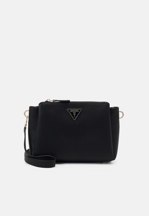Pochette Guess en cuir noir avec plaque logo argentée et fermeture éclair sur un fond clair uni.