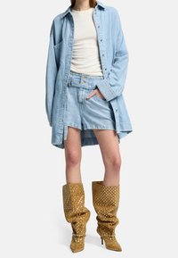 Camisa de denim oversized azul claro,-top blanco ajustado, pantalones cortos azul claro y botas hasta la rodilla con lunares amarillos y punta afilada.