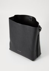 Borsa in pelle nera con texture granulosa, design a apertura superiore e chiusura a pressione. Branding minimalista sul davanti. Forma rettangolare.