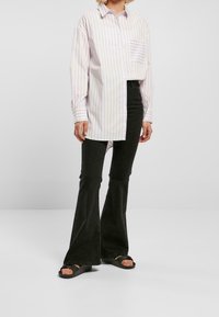 Chemise à rayures boutonnée en violet pâle et blanc, avec une poche ; associée à un jean évasé noir et des sandales plates noires.