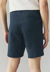 Shorts pentru bărbați de culoare albastru marin, dintr-un material ușor, având două buzunare la spate cu închidere prin buton și un tiv drept.