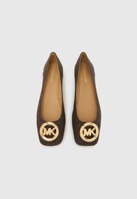 Καφέ υφασμάτινα μπαλαρίνια με τετράγωνη μύτη και έντονο χρυσό κυκλικό λογότυπο MK στο κουτί της μύτης. Το εσωτερικό είναι σε ταμπά χρώμα.